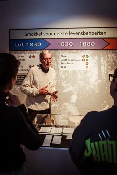 Een vrijwillige gids vertelt een groep over smokkel voor eerste levensbehoeften, voor een tijdlijnwand