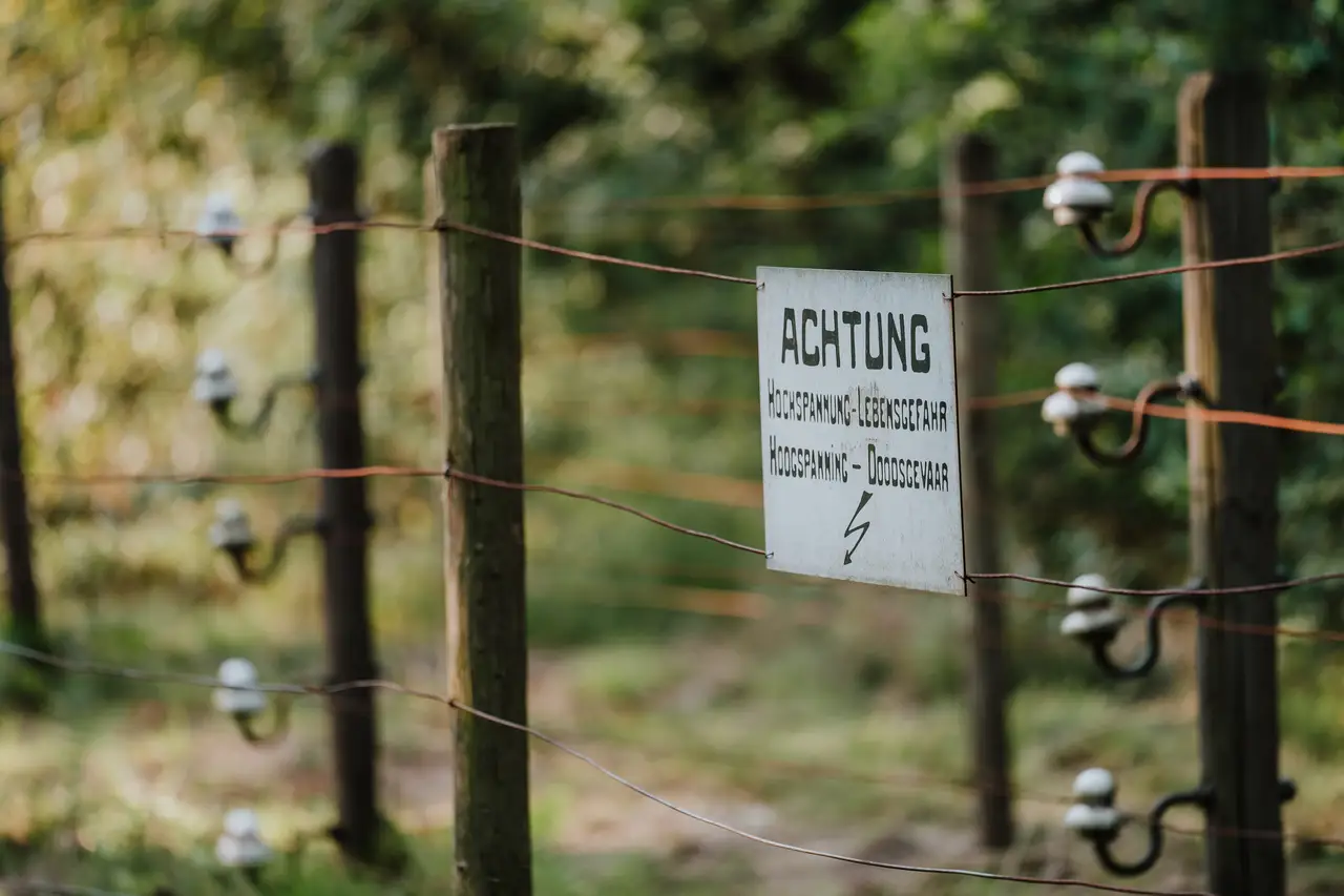 Nagebouwde Doodendraad bij de Achelse Kluis: draden met isolatoren en een bord ‘Achtung, Hochspannung – Lebensgefahr’