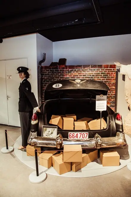 De zwarte Amerikaanse jaren-vijftigauto van het museum, de kofferbak vol smokkelwaar, met een douanepop ernaast